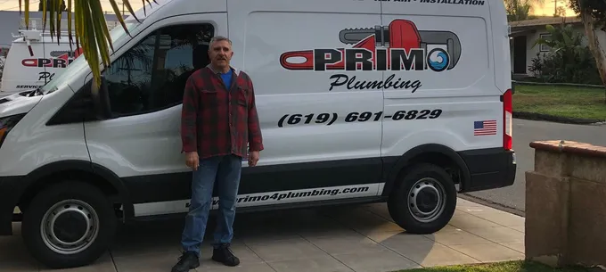 A Primo Plumbing technician beside the company's branded van in a driveway, with the shop's phone number on the side