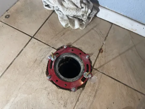 A newly installed toilet flange with a metal repair ring secured over a drain opening in a tiled bathroom floor