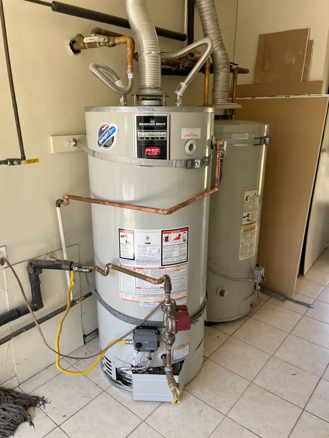 A newly installed gas water heater with copper piping, flexible vent connectors, and seismic strapping in a garage — neat, code-conscious work by Primo Plumbing